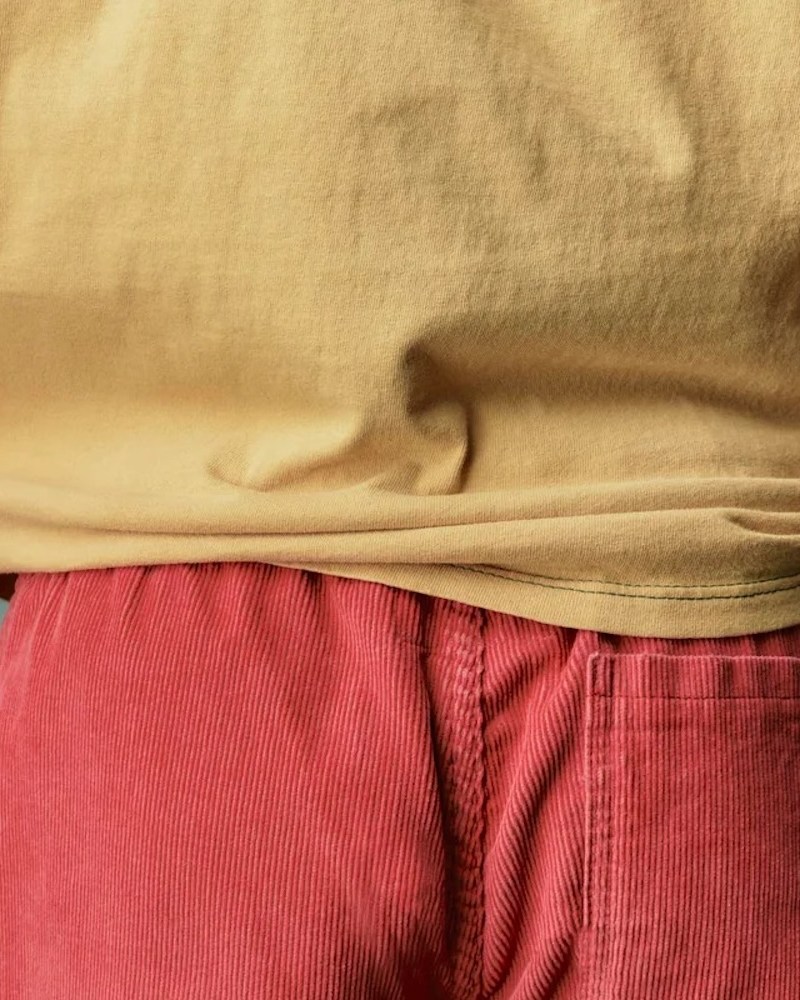 A model wearing a yellow shirt and red cord shorts.