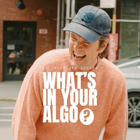 A man in a peach sweater with a New York Rangers baseball cap laughing, with the text "What's in Your Algo?" over the top