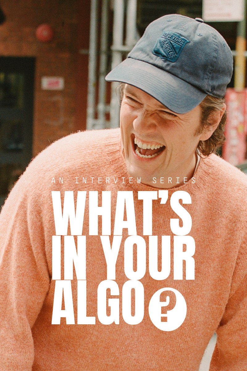 A man in a peach sweater with a New York Rangers baseball cap laughing, with the text "What's in Your Algo?" over the top