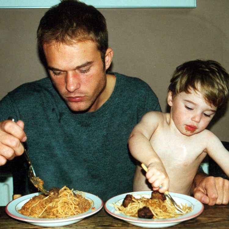 a father and small son eating bowls of spaghetti and meatballs at a wooden table