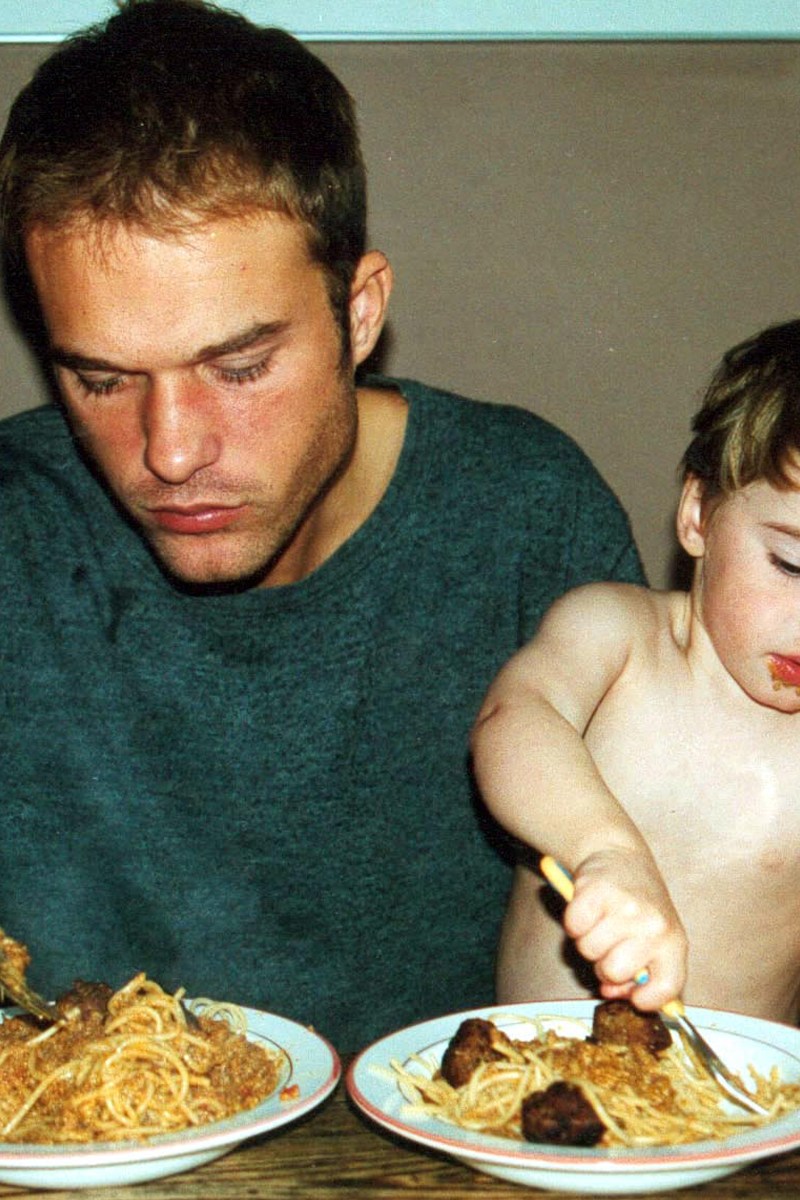 a father and small son eating bowls of spaghetti and meatballs at a wooden table