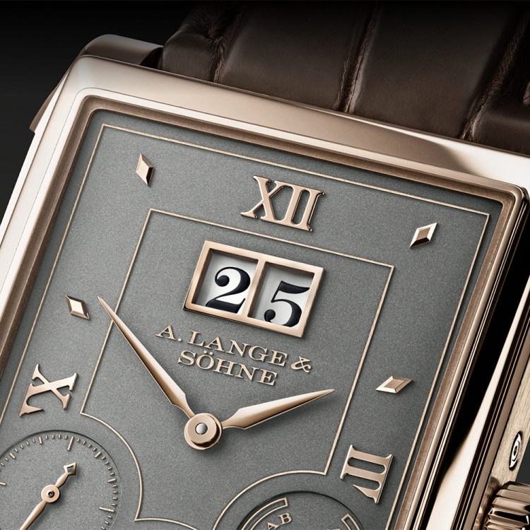 A close-up view of a watch dial with a golden bezel, grey dial and calendar windows with the numbers 25