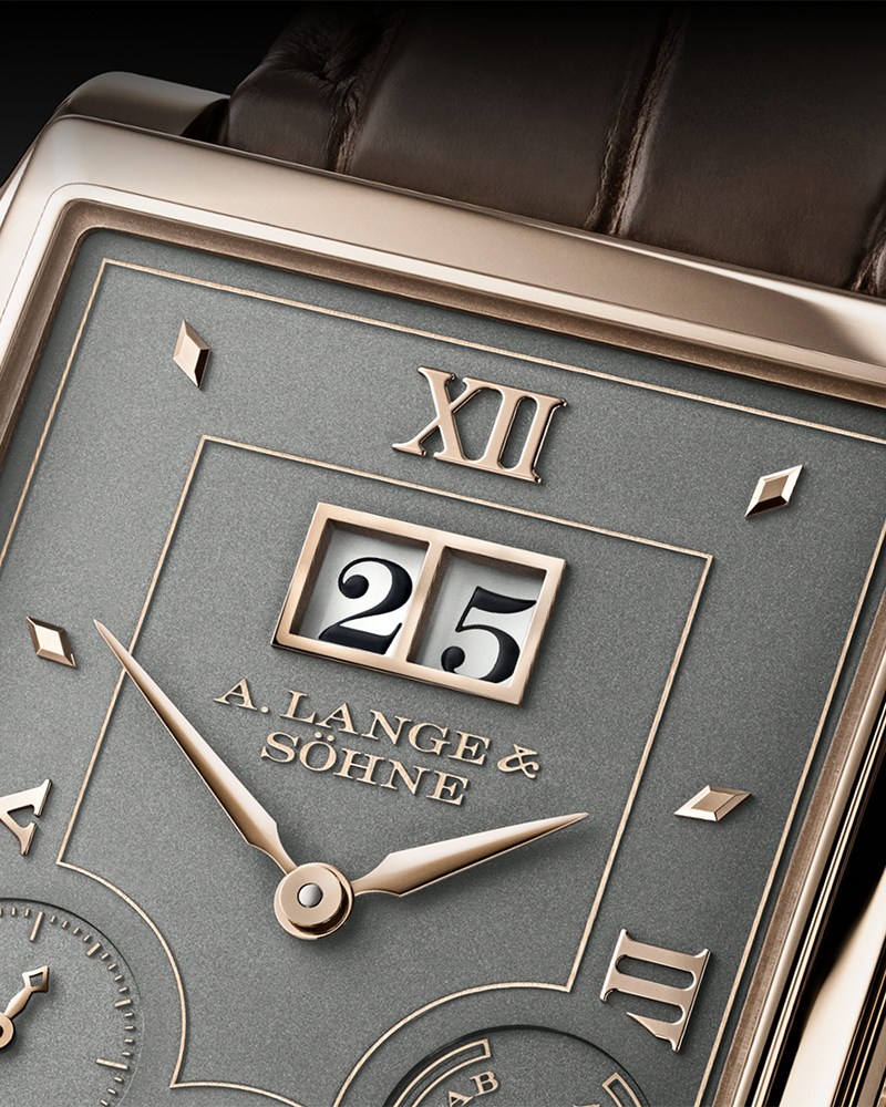 A close-up view of a watch dial with a golden bezel, grey dial and calendar windows with the numbers 25