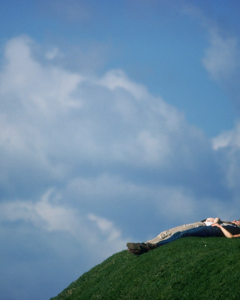 A couple resting on a hill under the sky.