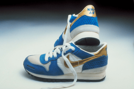Pair of vintage Nike Air sneakers in blue, white, and gold, one standing upright behind the other.
