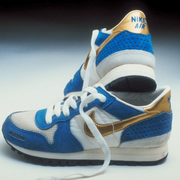 Pair of vintage Nike Air sneakers in blue, white, and gold, one standing upright behind the other.