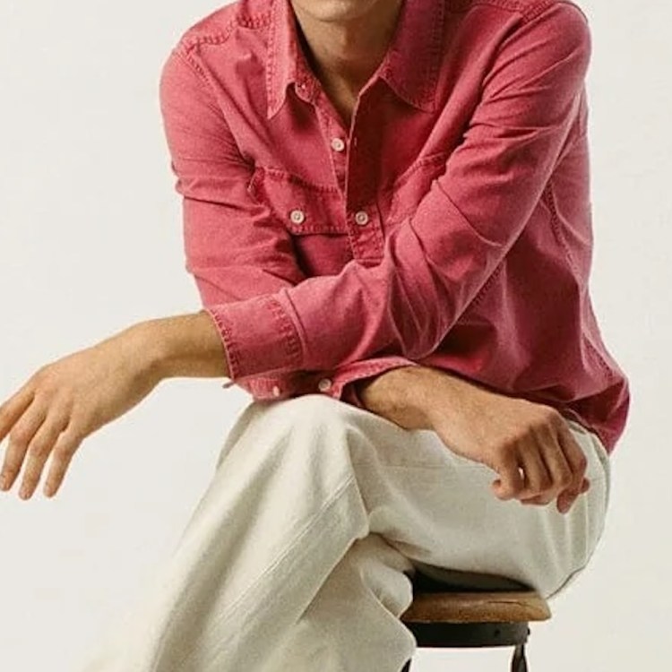 A model sitting on a tall stool in a light red shirt and white pants