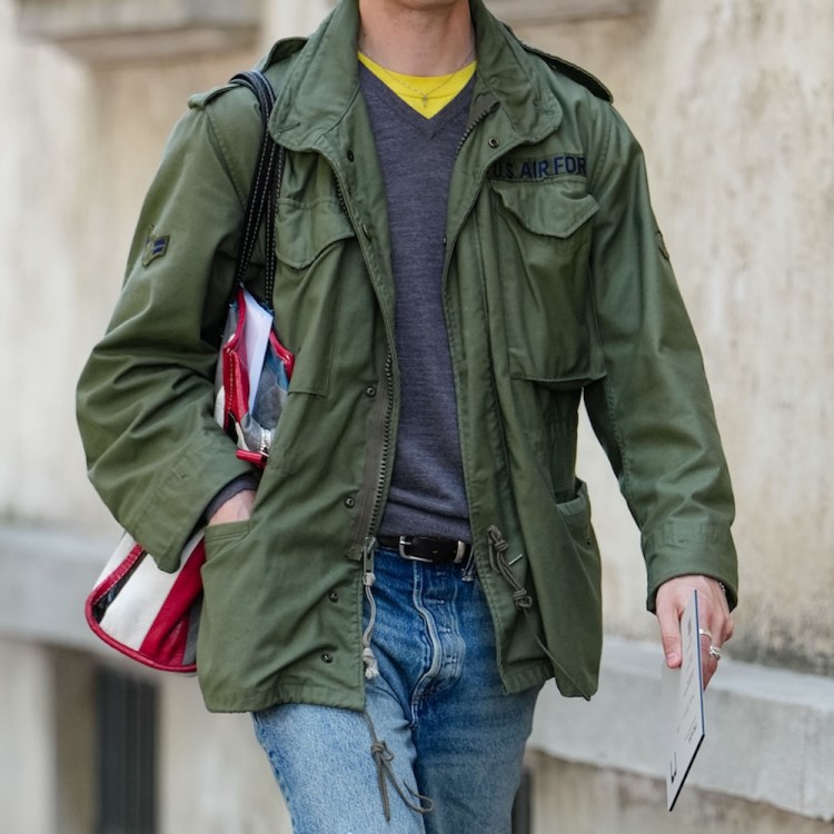 A man wearing dark yellow gray long sleeve sweater, dark green cargo jacket, navy blue ripped baggy denim jean pants, shiny black oxford moccasin leather shoes