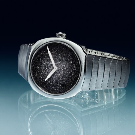 A stainless steel watch with two hands and a silver dial that fades from dark to light on a black and blue background