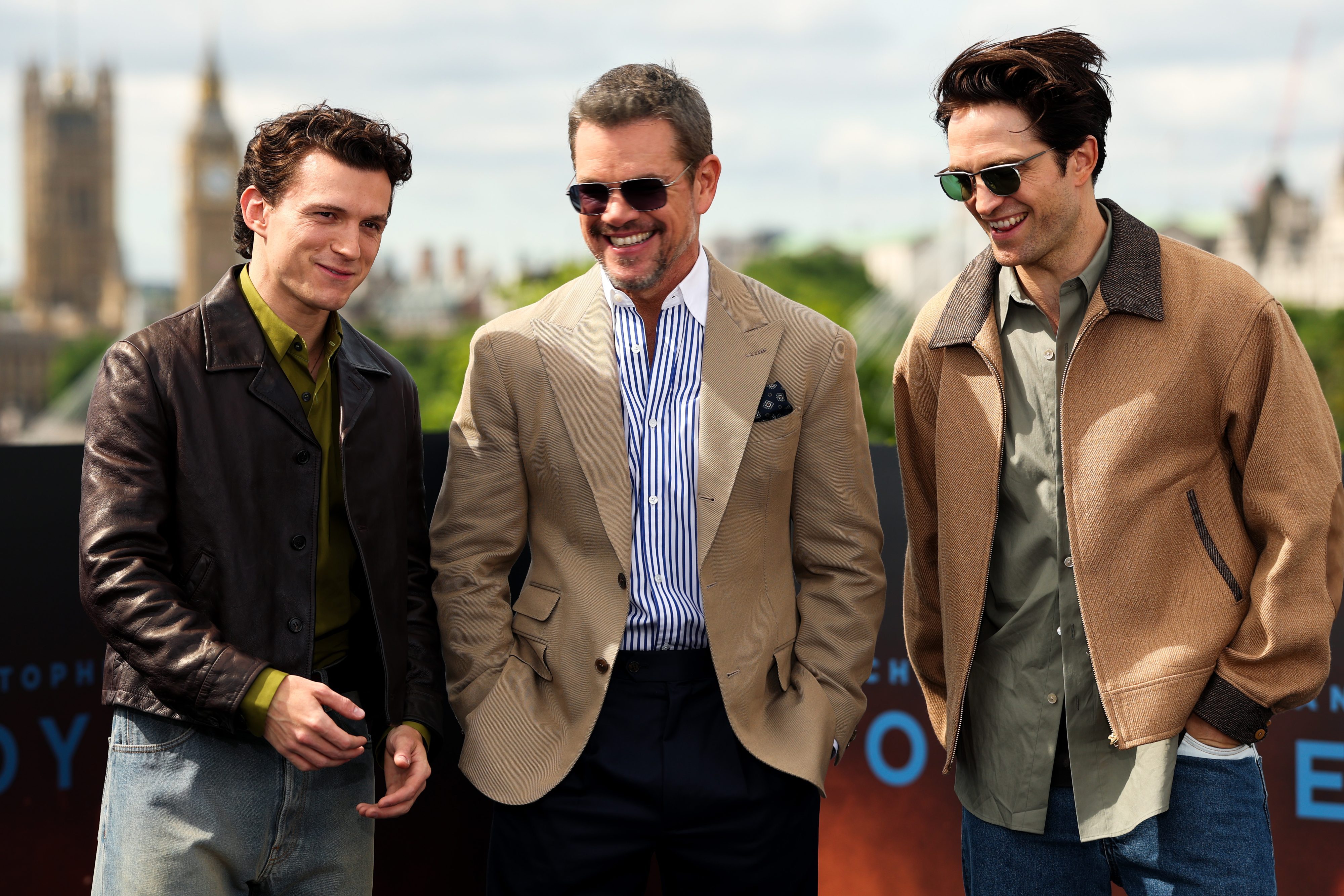 Actors Tom Holland, Matt Damon and Robert Pattinson standing in a line and smiling for a photo