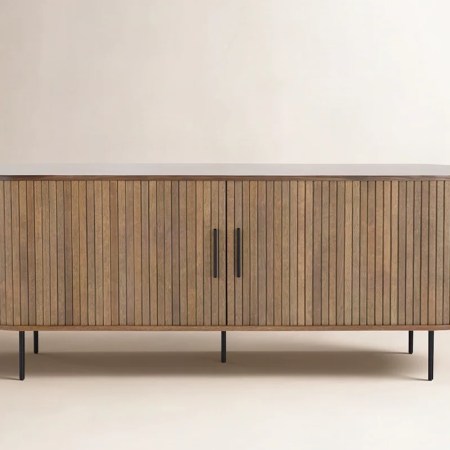 Oval wooden sideboard with vertical slats, two doors, black handles, and thin black legs.