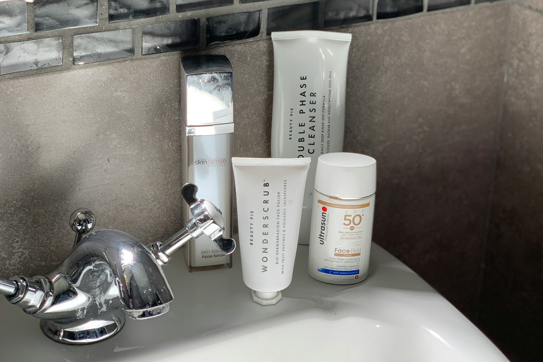 Skincare products on a bathroom sink: a silver bottle, two white tubes, and a white bottle of SPF 50.