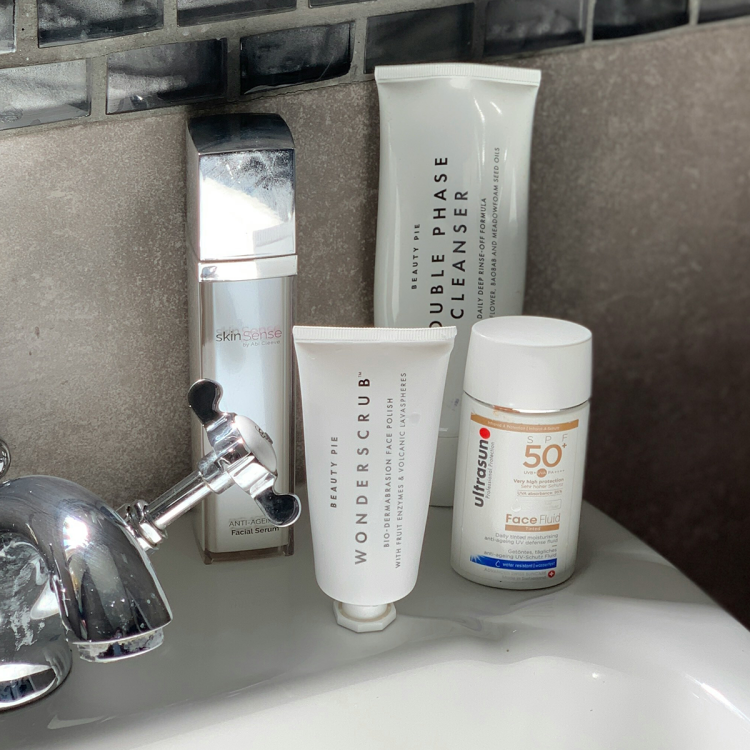 Skincare products on a bathroom sink: a silver bottle, two white tubes, and a white bottle of SPF 50.