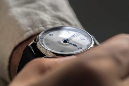 Close-up of a person's wrist wearing a silver watch with a white face, blue hands, and blue numbers.