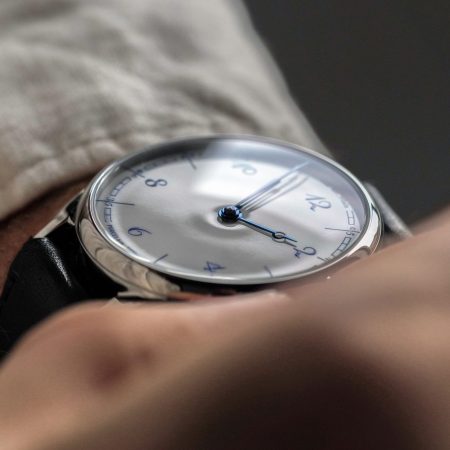 Close-up of a person's wrist wearing a silver watch with a white face, blue hands, and blue numbers.