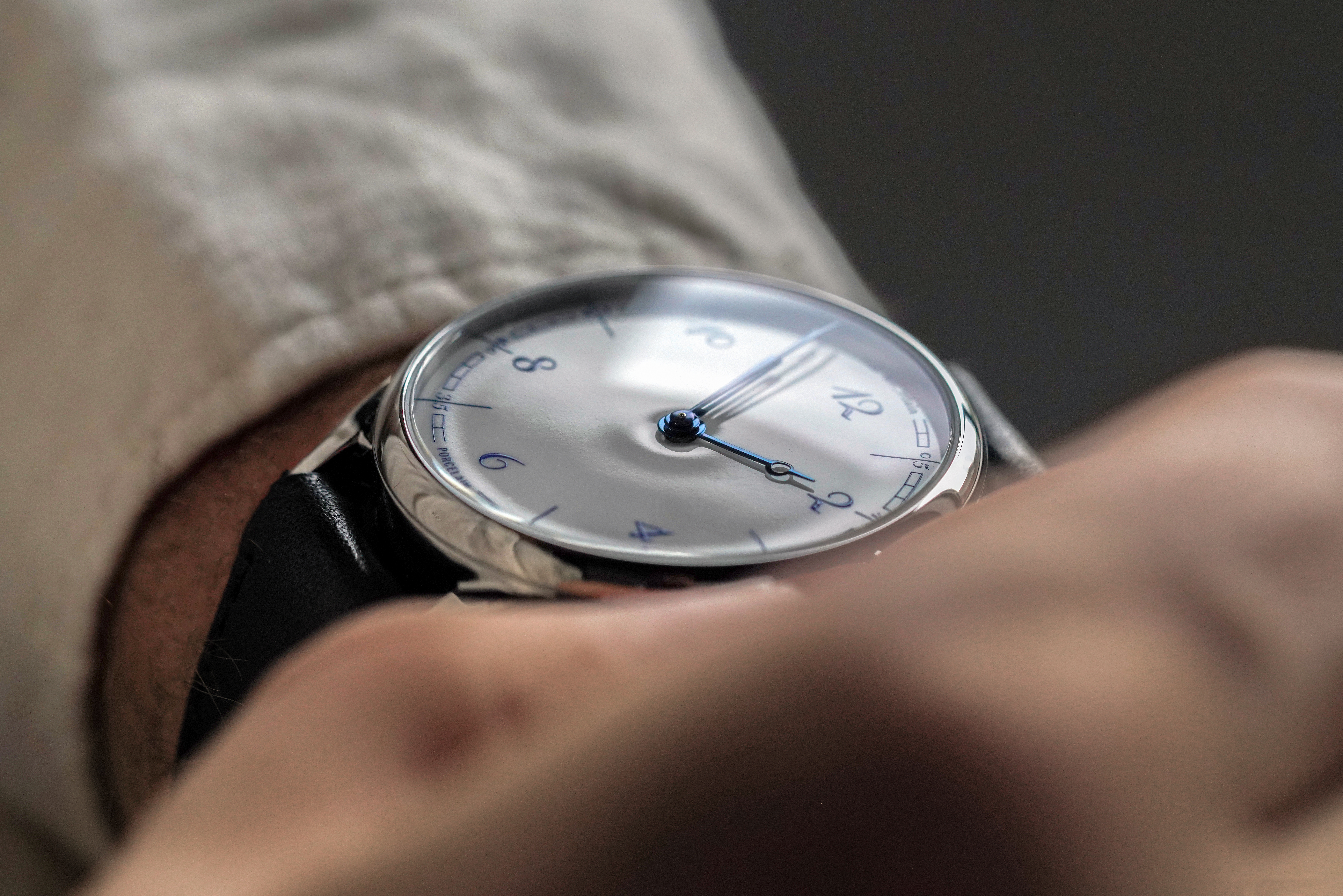 Close-up of a person's wrist wearing a silver watch with a white face, blue hands, and blue numbers.
