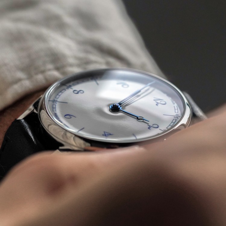 Close-up of a person's wrist wearing a silver watch with a white face, blue hands, and blue numbers.