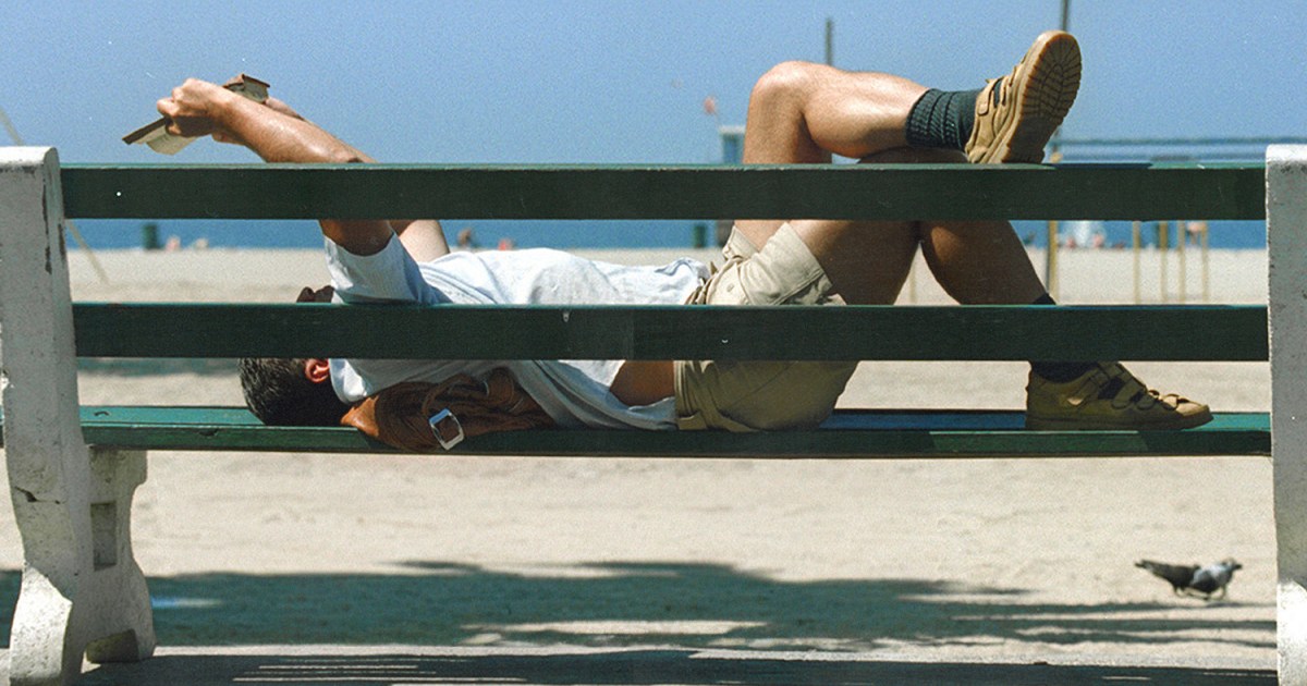 a man reading on a bench by the beach.