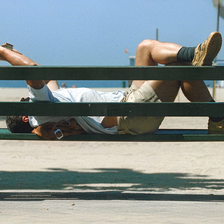 a man reading on a bench by the beach.
