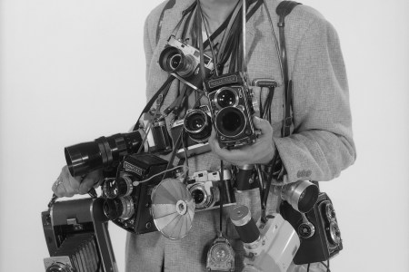 a man holding many old cameras against a white background.
