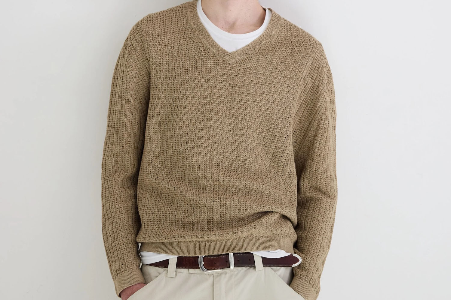 a model in a tan sweater over a white t-shirt against a white wall