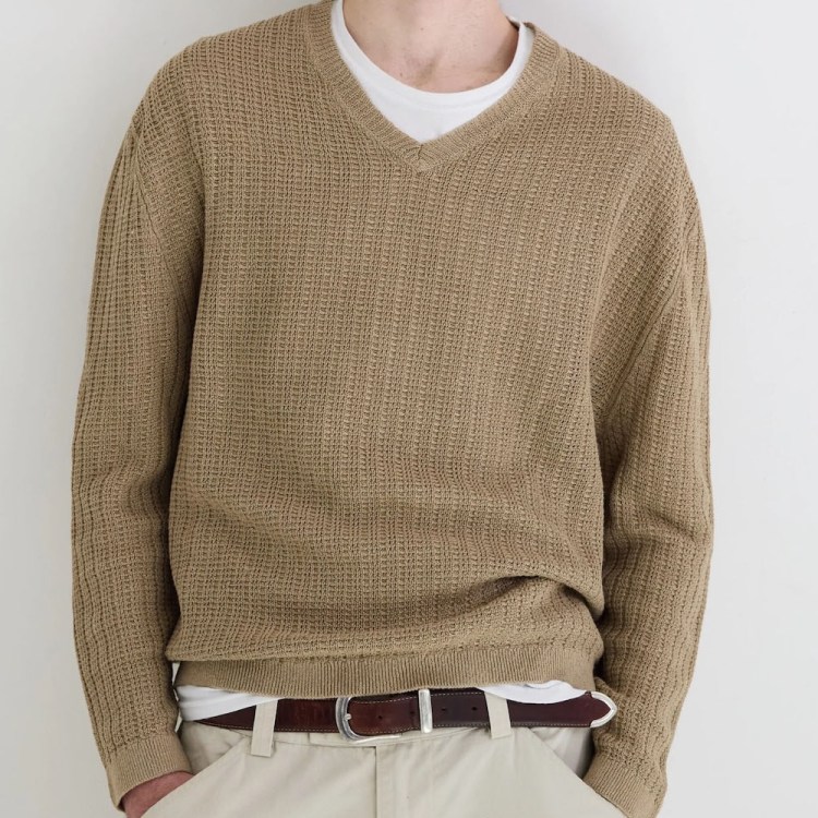 a model in a tan sweater over a white t-shirt against a white wall