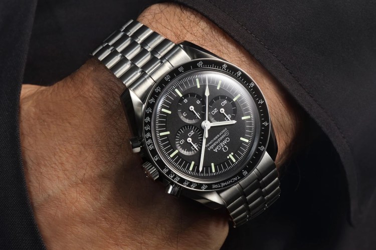 A man's wrist wearing an Omega Speedmaster Professional watch with a black dial and steel bracelet.