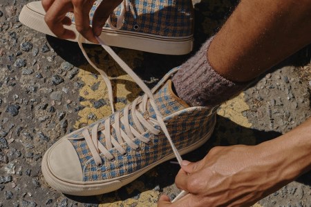 A model tying a pair of brown checked high-top sneakers.