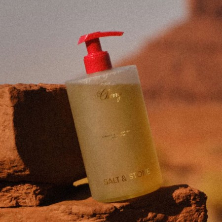 a bottle of body wash with a red cap on a rock in the desert.