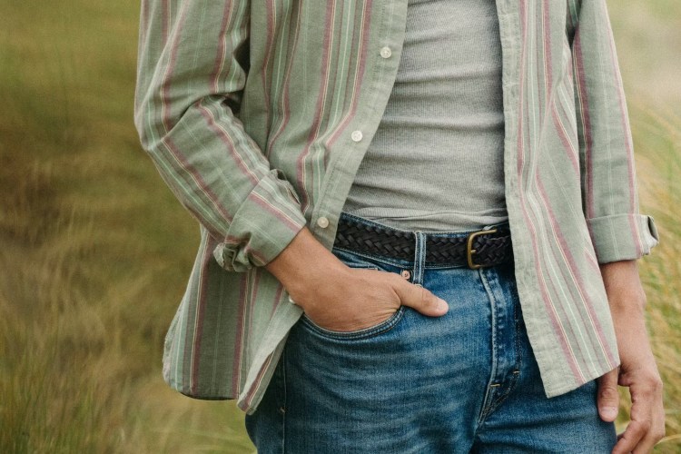 a model in a grey tank top, blue jeans and an open green button up
