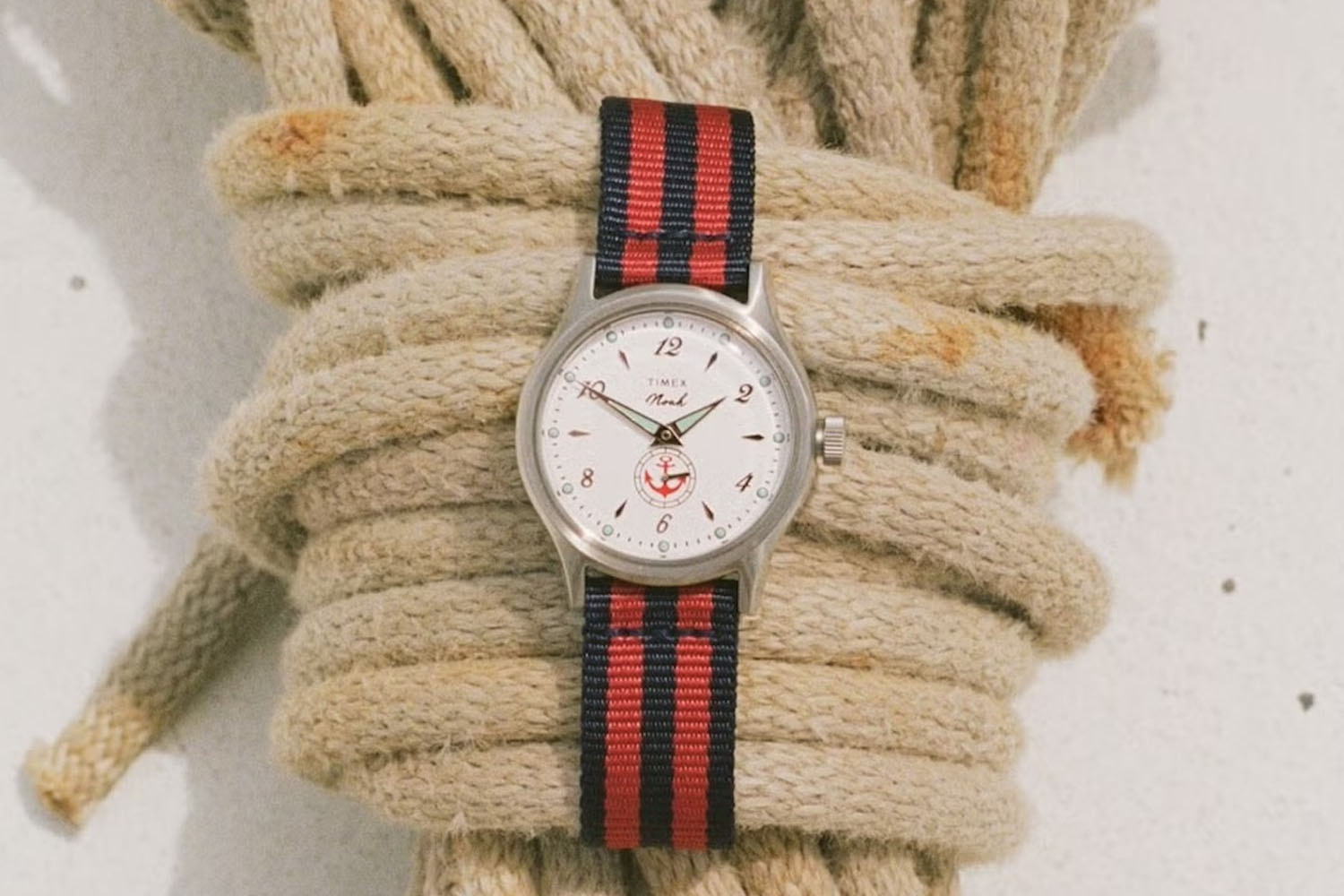 Silver watch with a cream face, red anchor logo, and a red and navy striped fabric strap.