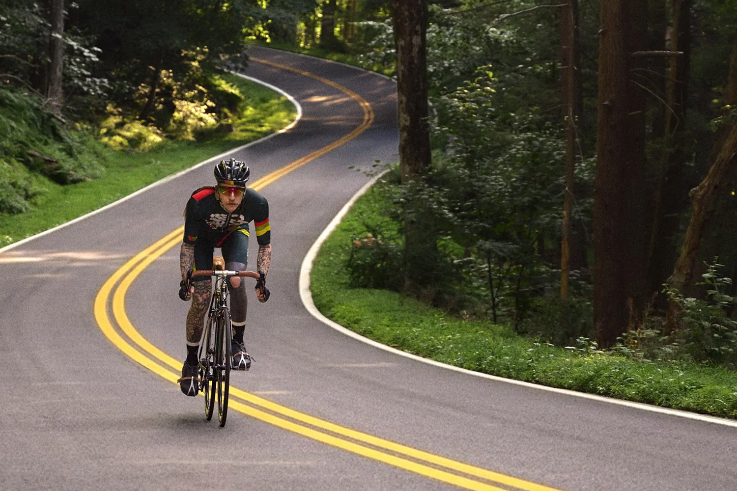 A man cycling on a long road in the woods.