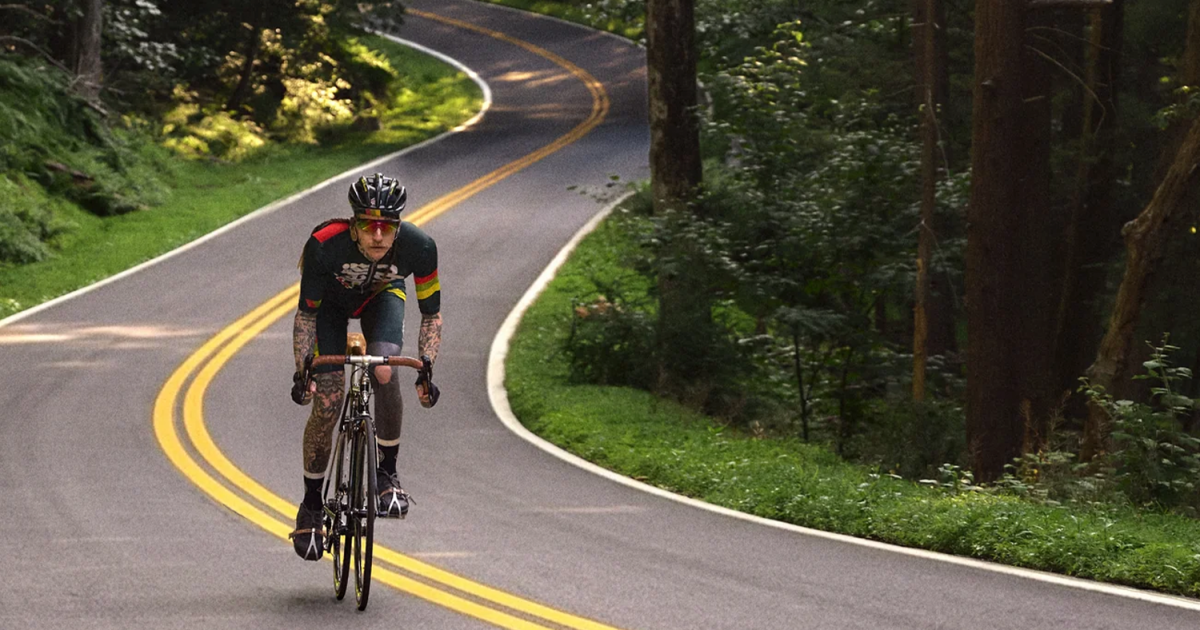A man cycling on a long road in the woods.