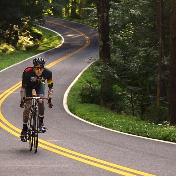 A man cycling on a long road in the woods.