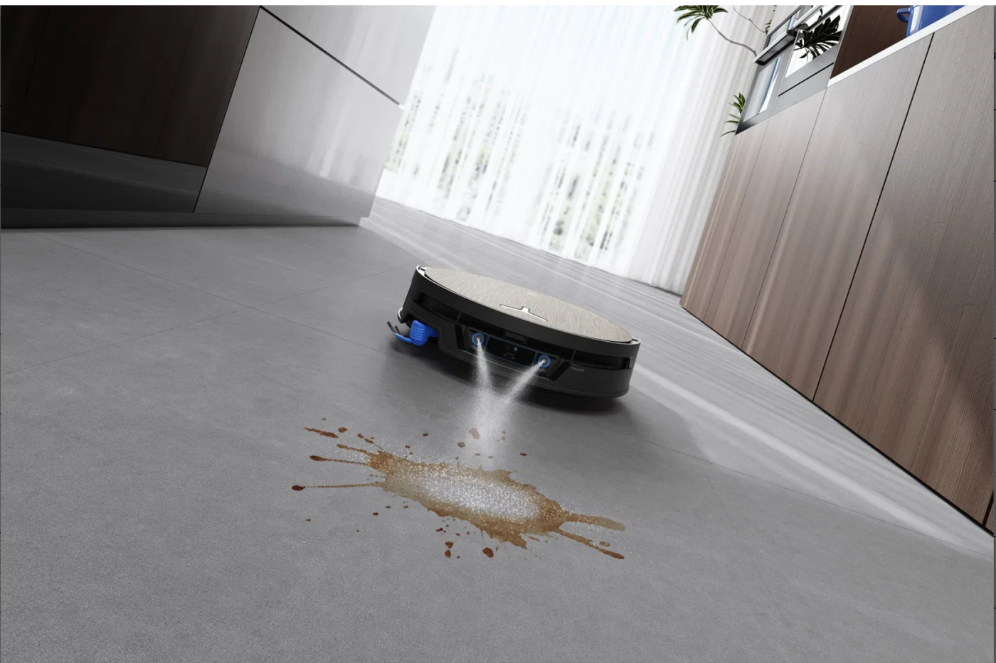 A black robotic vacuum cleaner spraying water onto a brown liquid spill on a gray floor in a modern kitchen.