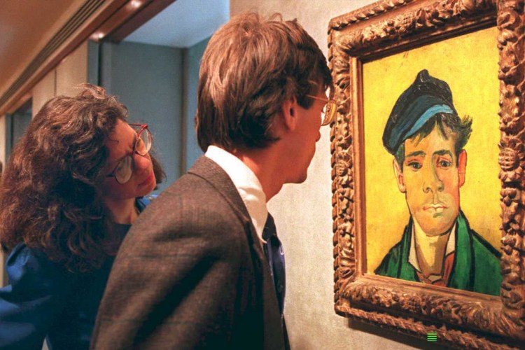 Two people, a man and a woman, look at a framed painting of a man with a blue cap and green jacket.