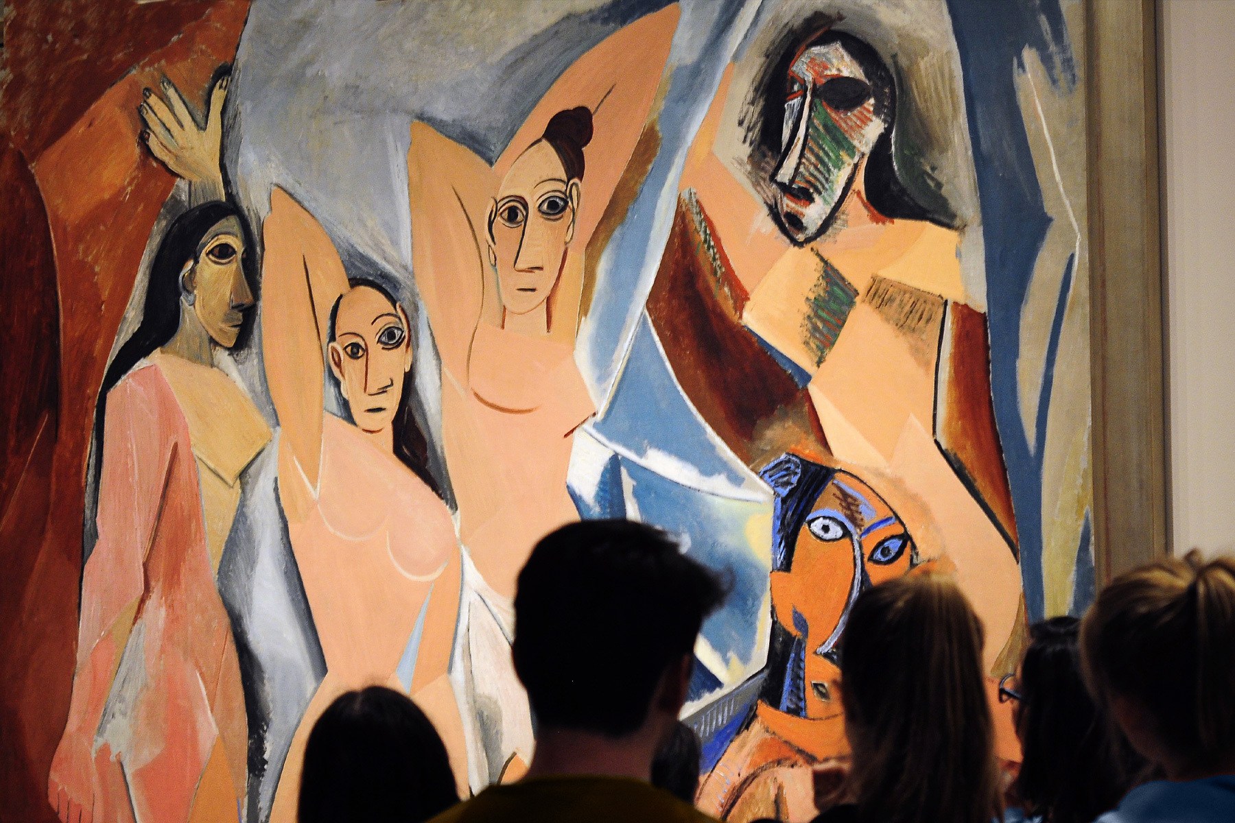 People viewing Picasso's "Les Demoiselles d'Avignon," a Cubist painting of five nude women with angular features.