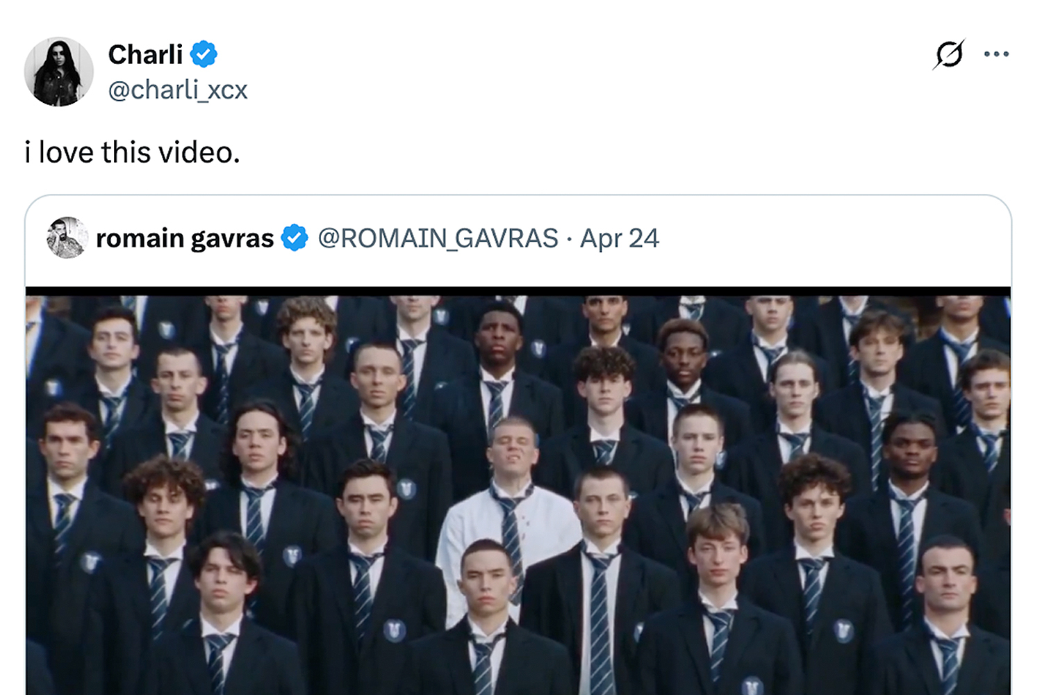 A screenshot of a tweet from Charli XCX featuring an image of a large group of young men in dark blazers and striped ties, one man in a white shirt stands out.