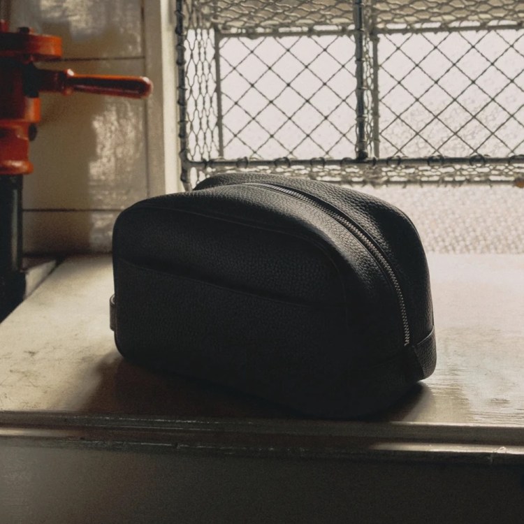 Black leather dopp kit on a worn counter, with an orange valve and a white mug in the background.