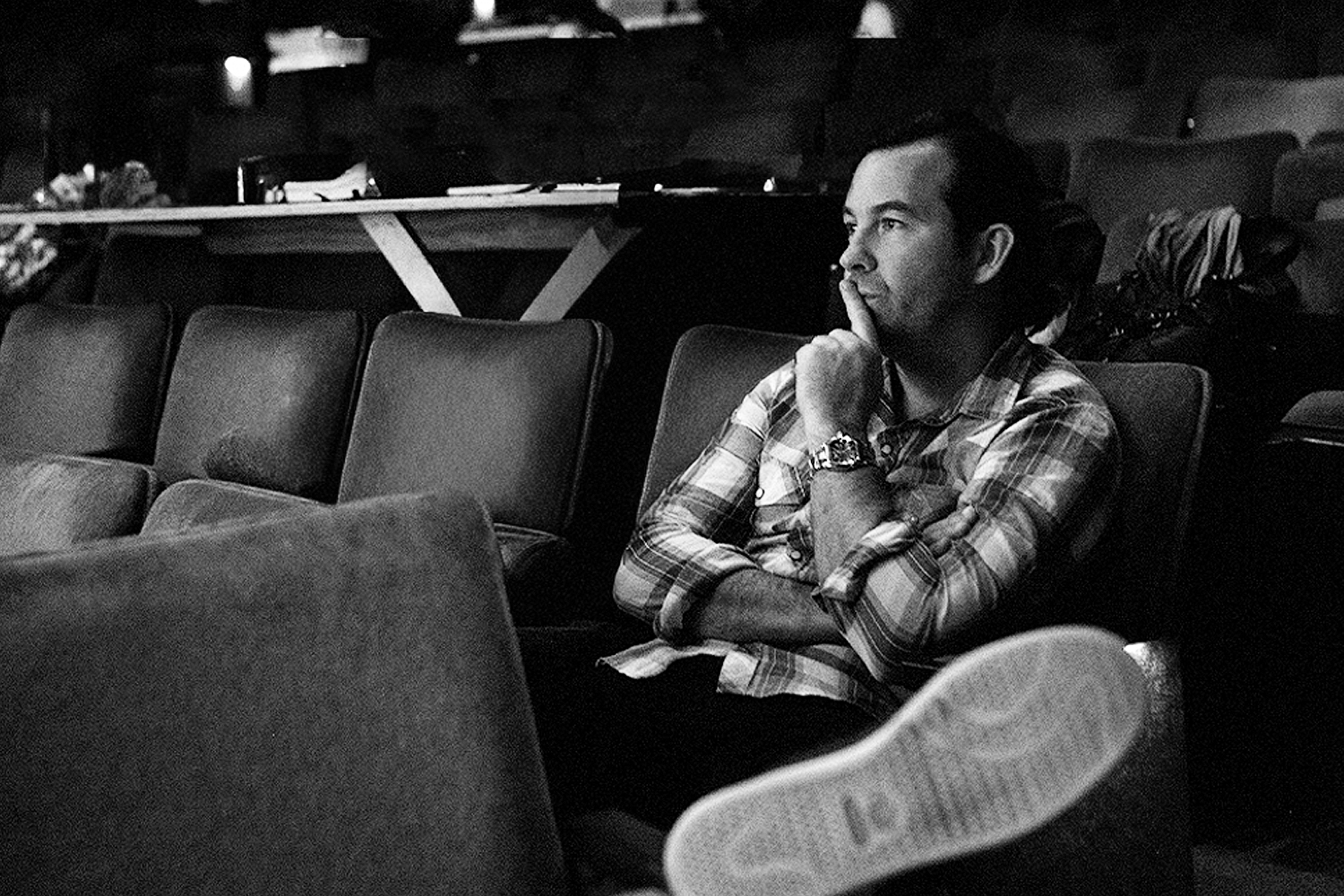 Black and white, Duncan Sheik in a plaid shirt sits in a theater, chin on hand, looking thoughtfully to the right.