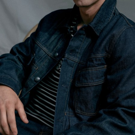 Person in a dark denim jacket and striped shirt, seated at a red table with a coffee cup.