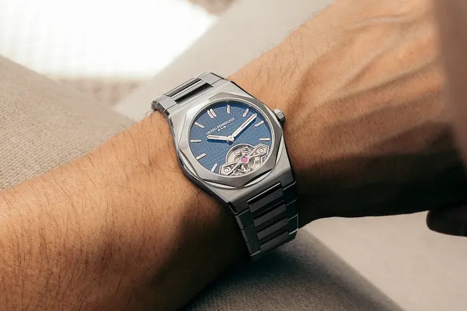 A person's arm wearing a silver Girard-Perregaux Laureato watch with a blue dial and visible tourbillon.