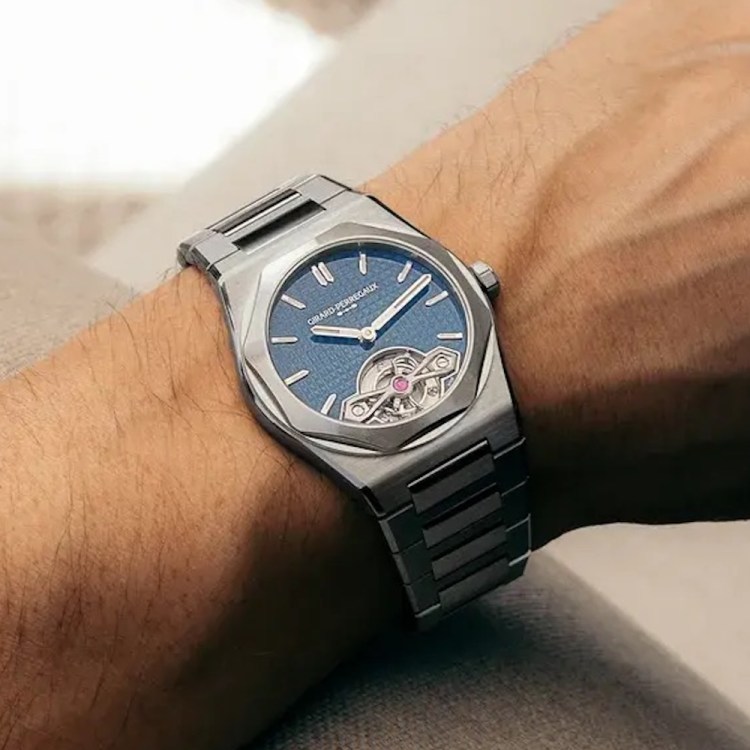 A person's arm wearing a silver Girard-Perregaux Laureato watch with a blue dial and visible tourbillon.