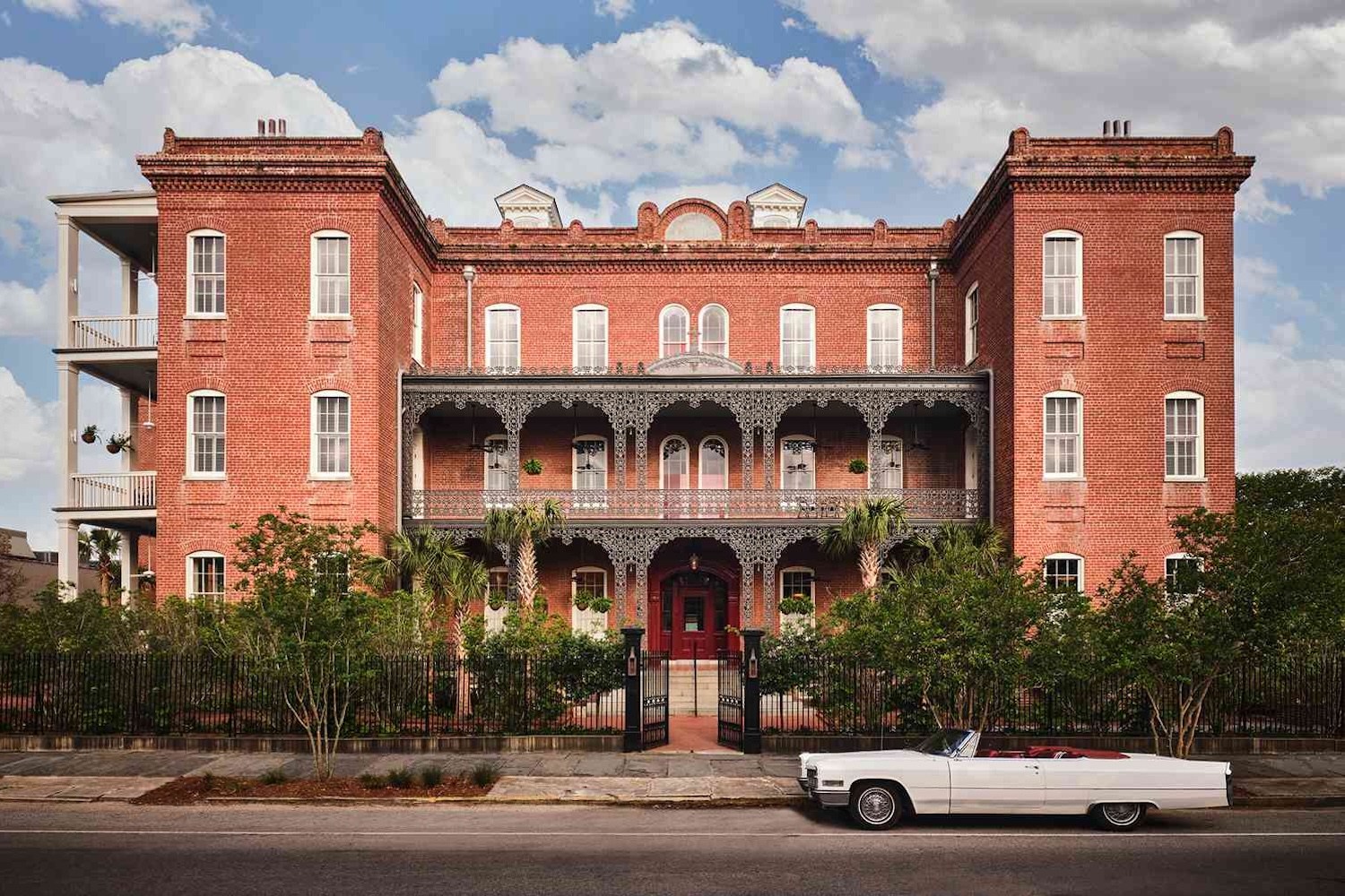 Grand red brick building with black iron balconies and a white vintage convertible parked on the street.