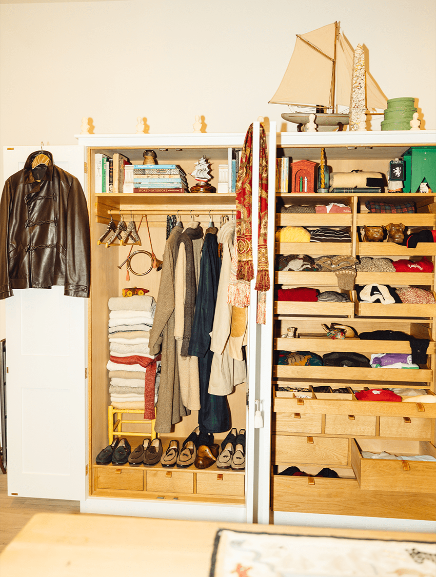 An open white wardrobe filled with neatly organized clothes, shoes, books, and decorative objects.
