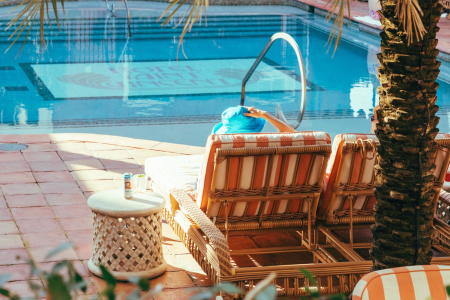 Person in a blue hat relaxing on a striped lounge chair by a pool with "Hotel Saint Vincent" visible at the bottom.