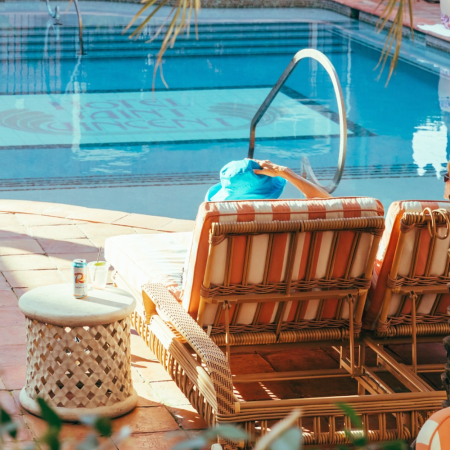 Person in a blue hat relaxing on a striped lounge chair by a pool with "Hotel Saint Vincent" visible at the bottom.