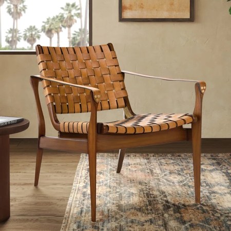 Woven leather and wood armchair next to a round side table with a book and glass, on a patterned rug.