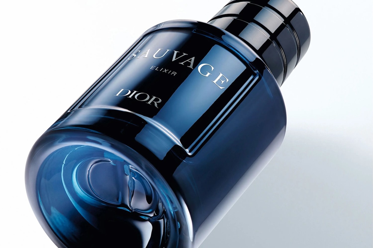 A dark blue glass bottle of Dior Sauvage Elixir cologne, tilted on a white background, with a black ribbed cap.