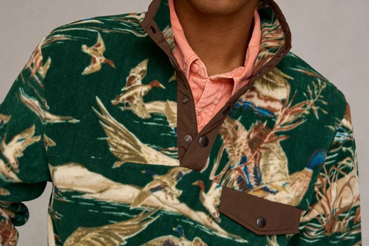 A person wearing a green fleece pullover with a duck hunting pattern, over a peach-colored collared shirt.